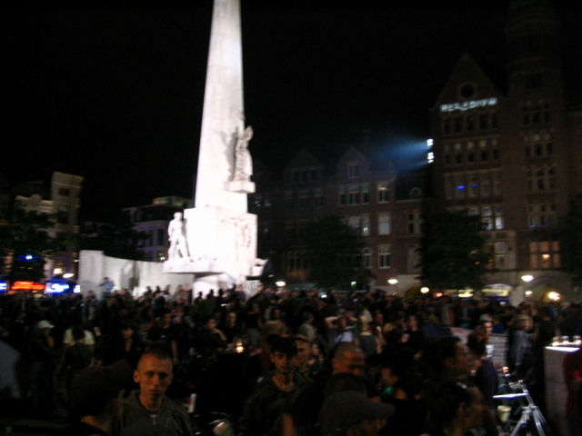 Het monument op de dam verlicht, met feestende mensen er omheen