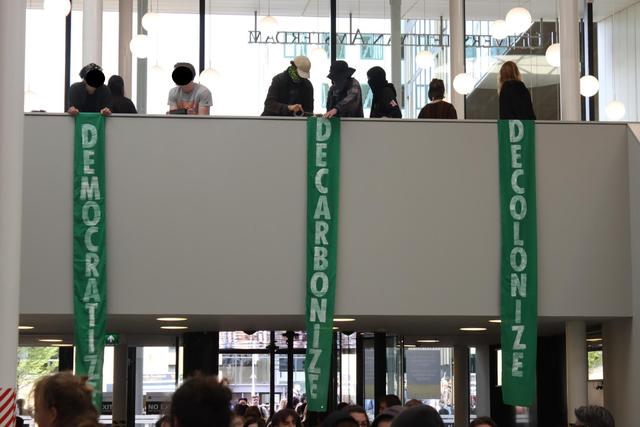 Drie banners met de teksten Democratize, Decolonize, Decarbonize