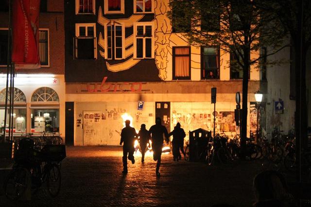 five people in black clothing running from burning tires in front of the ubica